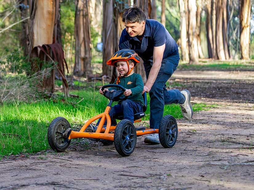Dad pushing their toddler on a bike through a nature trail