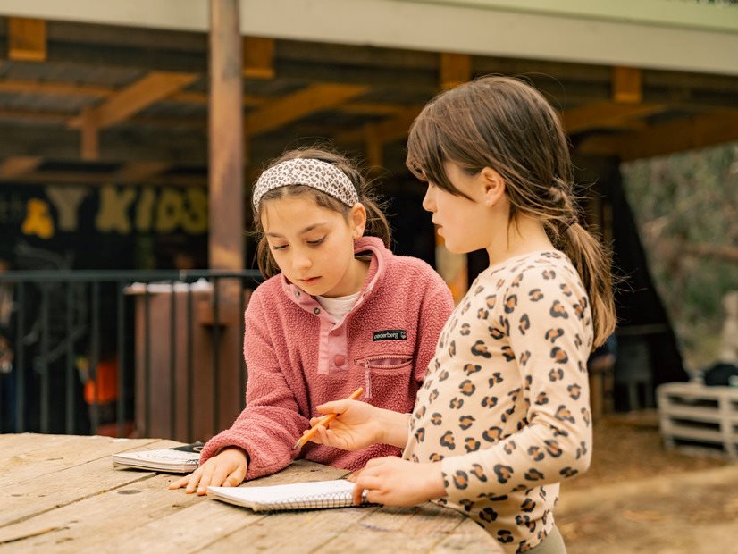 Two girls writing in a notepad at the Y's Forest Skills program