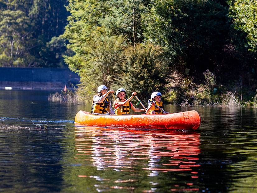 Three children in a canoe on a scenic lake at the Y Discovery Camps