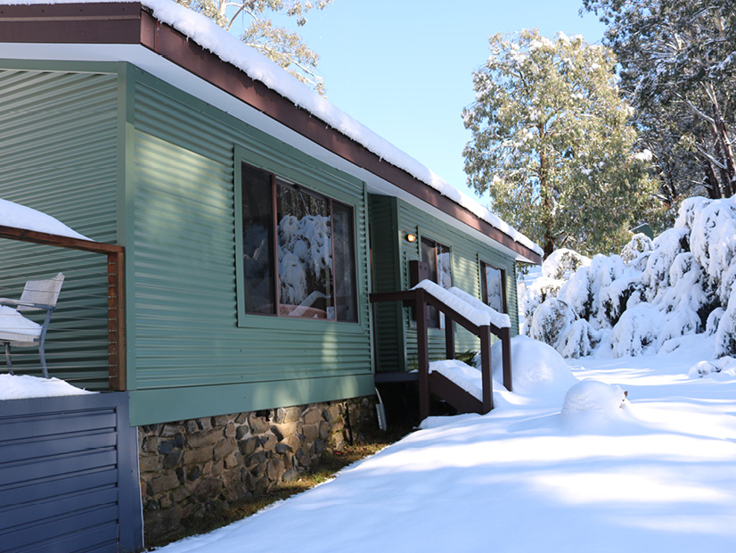 An exterior image of a private cottage at Howmans Gap Alpine Centre during snowfall.