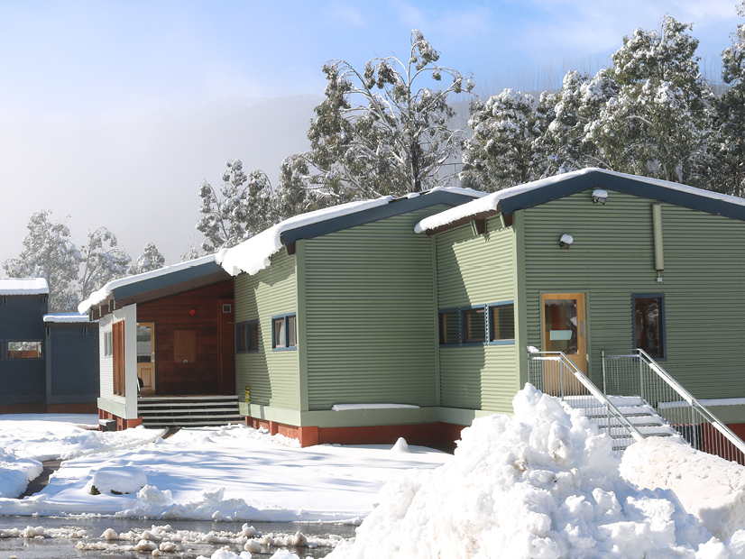 Exterior image of a large green building surrounded by trees and snow.