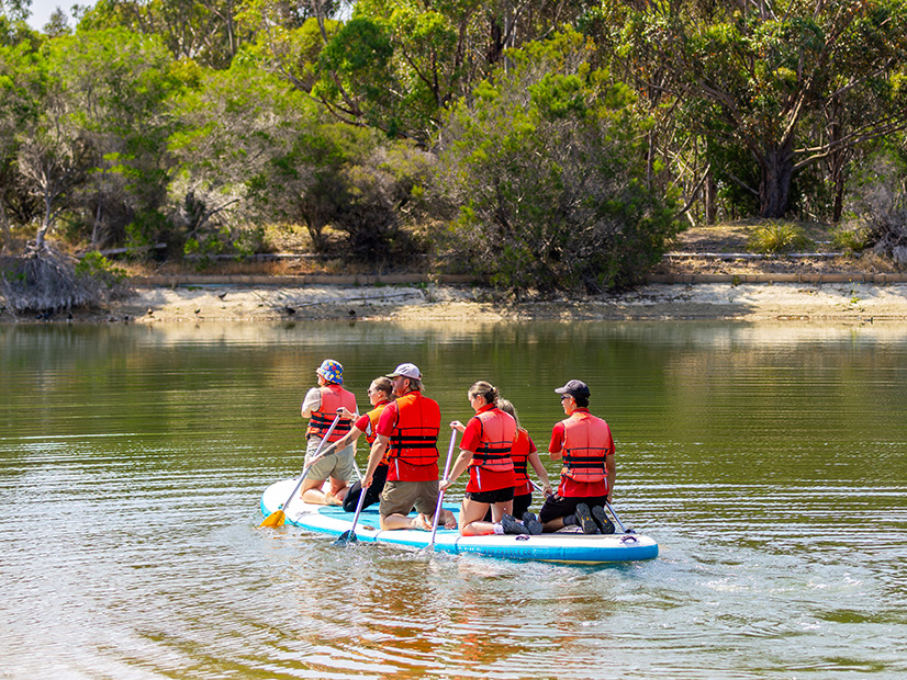 Group of six adults kneeling on a paddle board at Lake Dewar Discovery Camp
